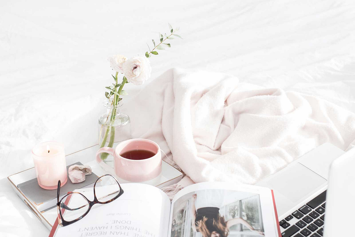 Open magazine, glasses and cup of coffee on bed